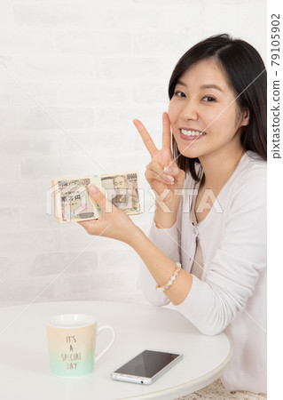 一位年輕女子通過智能手機信息賺了很多錢，手裡拿著一疊鈔票 79105902