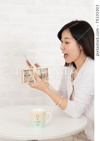 一位年輕女子通過智能手機信息賺了很多錢，手裡拿著一疊鈔票 79105903