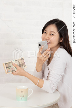 A young woman who gets a lot of money with smartphone information and holds a wad of bills 79105905