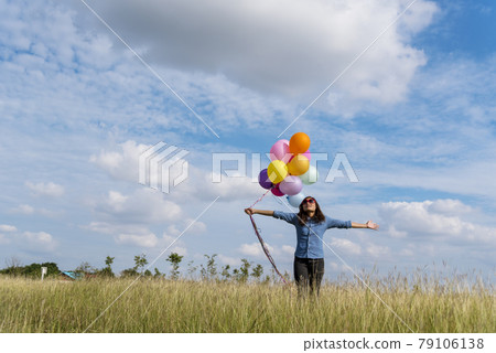 Woman holding balloons running on green meadow white cloud and blue sky with happiness Cheerful and relax. Hands holding vibrant air balloons play on birthday party happy times summer sunlight outdoor Woman holding balloons running on green meadow white cloud and blue sky with happiness Cheerful and relax. Hands holding vibrant air balloons play on birthday party happy times summer sunlight outdoor 79106138