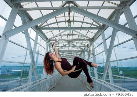 The red-haired aerial gymnast in a sports combo performs at the air hoop in a pedestrian crossing. The red-haired aerial gymnast in a sports combo performs at the air hoop in a pedestrian crossing. 79106453