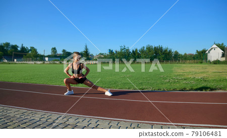 Young woman practicing side lunges at stadium. Young woman practicing side lunges at stadium. 79106481