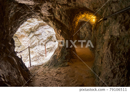 Poorly lit tunnel next to the narrow path along a gorge through the mountains of the Alps in the south of Germany at the border to Austria. Poorly lit tunnel next to the narrow path along a gorge through the mountains of the Alps in the south of Germany at the border to Austria. 79106511