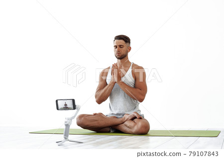 Fit Caucasian male recording a blog or streaming yoga workout. Fit Caucasian male recording a blog or streaming yoga workout. 79107843