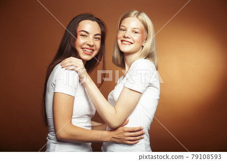 two pretty diverse girls happy posing together: blond and brunette, caucasian and asian on brown background, lifestyle people concept two pretty diverse girls happy posing together: blond and brunette, caucasian and asian on brown background, lifestyle people concept 79108593