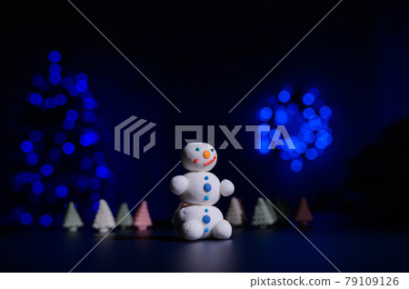 Cute snowman and little Christmas trees made of marshmallows on the background of Christmas lights. Garland of light bulbs on a tree. Happy new year. Cute snowman and little Christmas trees made of marshmallows on the background of Christmas lights. Garland of light bulbs on a tree. Happy new year. 79109126