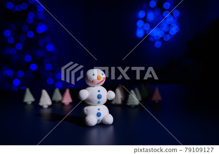 Cute snowman and little Christmas trees made of marshmallows on the background of Christmas lights. Garland of light bulbs on a tree. Happy new year. Cute snowman and little Christmas trees made of marshmallows on the background of Christmas lights. Garland of light bulbs on a tree. Happy new year. 79109127
