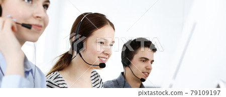 Casual dressed young woman using headset and computer while talking with customers online. Group of operators at work. Call center, business concept Casual dressed young woman using headset and computer while talking with customers online. Group of operators at work. Call center, business concept 79109197