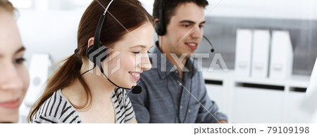 Casual dressed young woman using headset and computer while talking with customers online. Group of operators at work. Call center, business concept Casual dressed young woman using headset and computer while talking with customers online. Group of operators at work. Call center, business concept 79109198