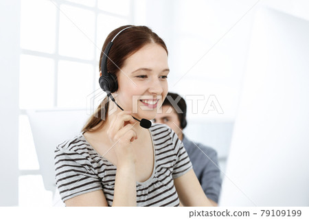 Casual dressed young woman using headset and computer while talking with customers online. Group of operators at work. Call center, business concept 79109199