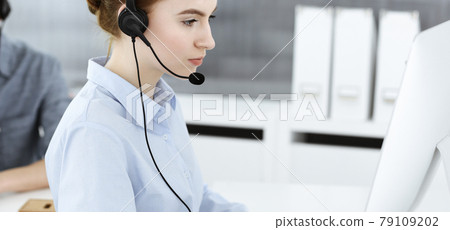 Young woman using headset and computer while talking with customers online. Group of Call center operators at work. Business concept Young woman using headset and computer while talking with customers online. Group of Call center operators at work. Business concept 79109202