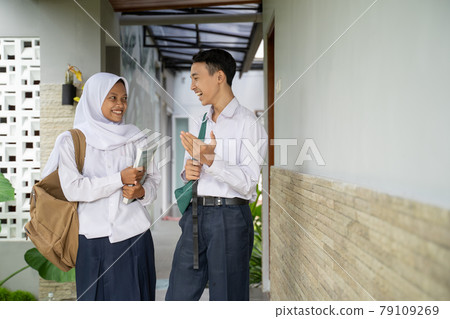 a male and female student in school uniform chatting together while carrying books a male and female student in school uniform chatting together while carrying books 79109269