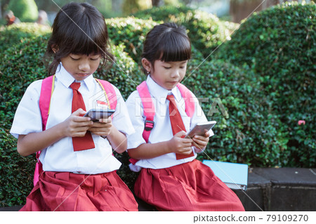 asian primary student using mobile phone in school park asian primary student using mobile phone in school park 79109270