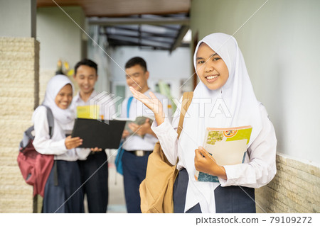 a young girl in a veil smiles at the camera with hand gestures in a school uniform carrying a school bag with copyspace a young girl in a veil smiles at the camera with hand gestures in a school uniform carrying a school bag with copyspace 79109272