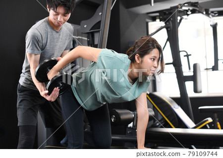 Asian women doing one-handed rowing (muscle training) and male trainers assisting Asian women doing one-handed rowing (muscle training) and male trainers assisting 79109744