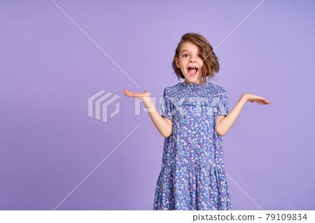 Photo of young happy surprised girl spread her hands to the sides isolated on purple color background Photo of young happy surprised girl spread her hands to the sides isolated on purple color background 79109834