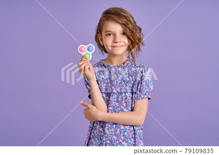 Picture of little girl with a modern popit toy. Colorful and bright pop it toy simple dimple. Trendy anti stress sensory toy fidget push pop it and simple dimple in kid's hands 79109835