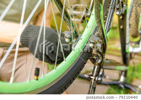 Bike mechanic man repairs bicycle in bicycle repair shop, outdoor. Hand of cyclist bicyclist examines, fixes modern cycle transmission system. Bike maintenance, sport shop concept. 79110440