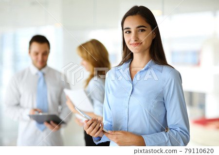 A friendly young businesswoman or female student is standing with some papers in the office. Lifestyle and diverse people concept 79110620