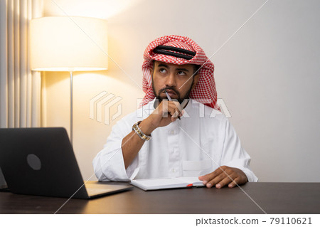 Arab businessman in turban thinking while writing at work desk Arab businessman in turban thinking while writing at work desk 79110621