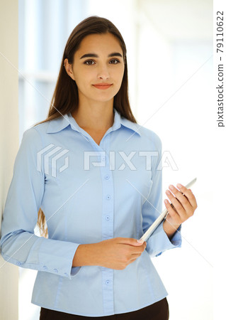 A friendly young businesswoman or female student is standing with some papers in the office. Lifestyle and diverse people concept 79110622