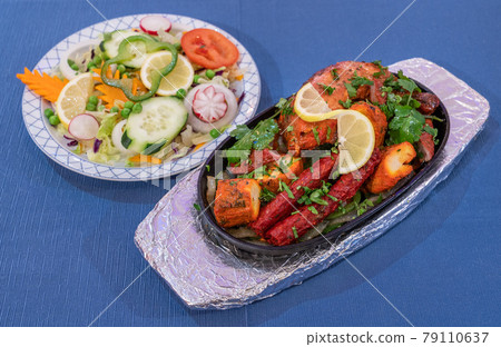 Mixed grilled meat with pepper sauce and vegetables on a blue background. Indian traditional cuisine. Mixed grilled meat with pepper sauce and vegetables on a blue background. Indian traditional cuisine. 79110637