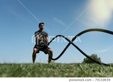 Male athlete on the outdoor in the park, exercises for endurance, using a thick rope, for cross fitness. European In summer Male athlete on the outdoor in the park, exercises for endurance, using a thick rope, for cross fitness. European In summer 79110639