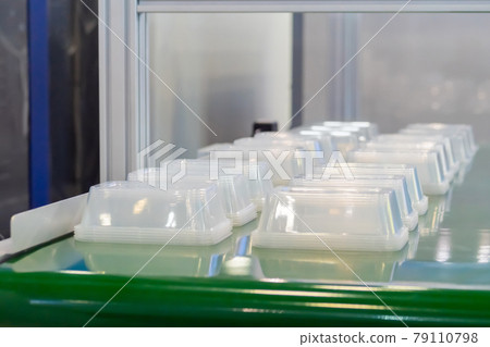 Empty food containers on conveyor belt of plastic injection molding machine Empty food containers on conveyor belt of plastic injection molding machine 79110798