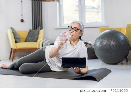 Elderly woman using tablet while training on yoga mat 79111063
