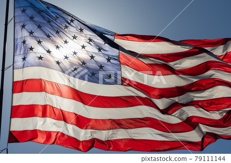 Backlit American Flag Waving In Wind Against a Deep Blue Sky 79111144