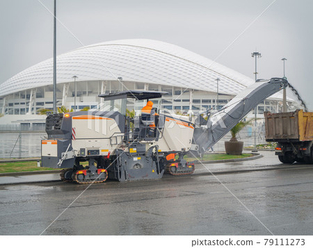 A road mill loads crushed asphalt into a dump truck on the background of a domed white building. Men at work 79111273