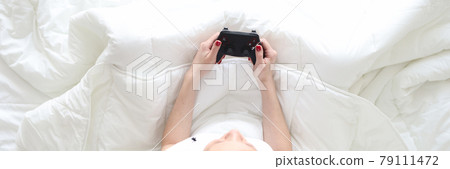 Woman sitting in bed with joystick in her hands top view 79111472