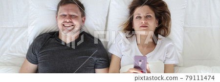 Young man and woman lying in bed and holding phone and joystick top view Young man and woman lying in bed and holding phone and joystick top view 79111474