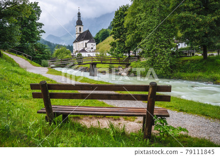 A wood bench with parish church, river abd mountains in background. berchtesgaden, Ramsau Germany A wood bench with parish church, river abd mountains in background. berchtesgaden, Ramsau Germany 79111845