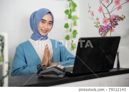 close up of a veiled business woman smiles with a greeting gesture while sitting in front of a laptop computer close up of a veiled business woman smiles with a greeting gesture while sitting in front of a laptop computer 79112143