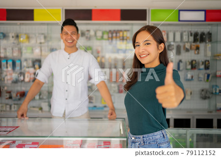 beautiful young woman with thumbs up standing against the background of a smartphone shop beautiful young woman with thumbs up standing against the background of a smartphone shop 79112152