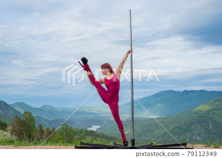 Beautiful red-haired woman dancing on a portable platform on a background of mountains. The girl moves next to the pole. Jumpsuit for classes. high heels. Altai. Awesome flexibility. Beautiful red-haired woman dancing on a portable platform on a background of mountains. The girl moves next to the pole. Jumpsuit for classes. high heels. Altai. Awesome flexibility. 79112349