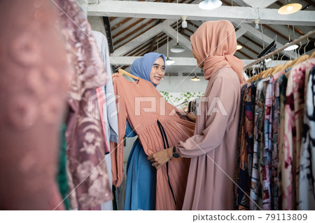 asian veiled waitresses while serving female shoppers choosing clothes on hangers asian veiled waitresses while serving female shoppers choosing clothes on hangers 79113809