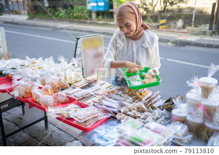 A beautiful girl in a headscarf holding a plastic tray to put fried options bought A beautiful girl in a headscarf holding a plastic tray to put fried options bought 79113810