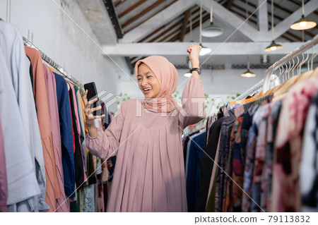a beautiful girl in a headscarf felt excited to raise her hand while holding a smartphone 79113832