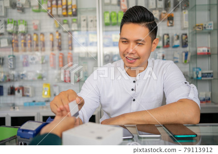 an entrepreneur man sitting behind a display case serving a mobile phone shopper an entrepreneur man sitting behind a display case serving a mobile phone shopper 79113912