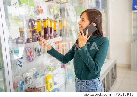 beautiful woman making a call with a smartphone while choosing cell phone accessories in a display case beautiful woman making a call with a smartphone while choosing cell phone accessories in a display case 79113915