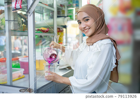 beautiful girl in hijab smiles at the camera holding a blender jar while pouring fruit juice 79113926