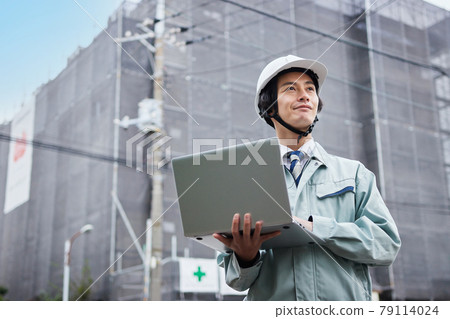 一個穿著工作服的人，看著在建築工地前的一台計算機 79114024