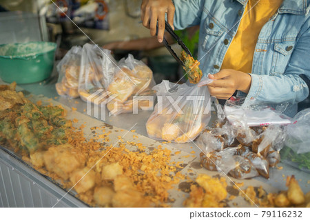 the seller uses tong tongs to take the fried food into a plastic wrapper 79116232