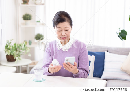 Senior woman comparing a bottle of supplements with a smartphone 79117758