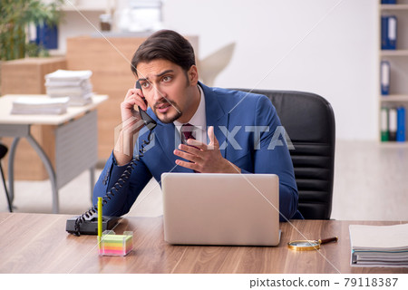 Young male employee sitting at workplace Young male employee sitting at workplace 79118387