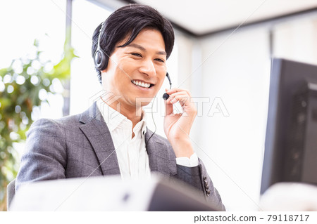 A man in a suit wearing a headset and heading to a desktop computer 79118717