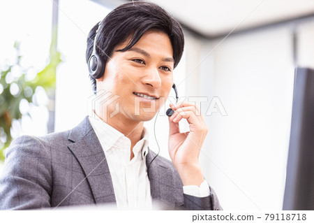 A man in a suit wearing a headset and heading to a desktop computer 79118718
