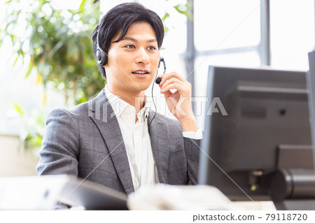 A man in a suit wearing a headset and heading to a desktop computer 79118720